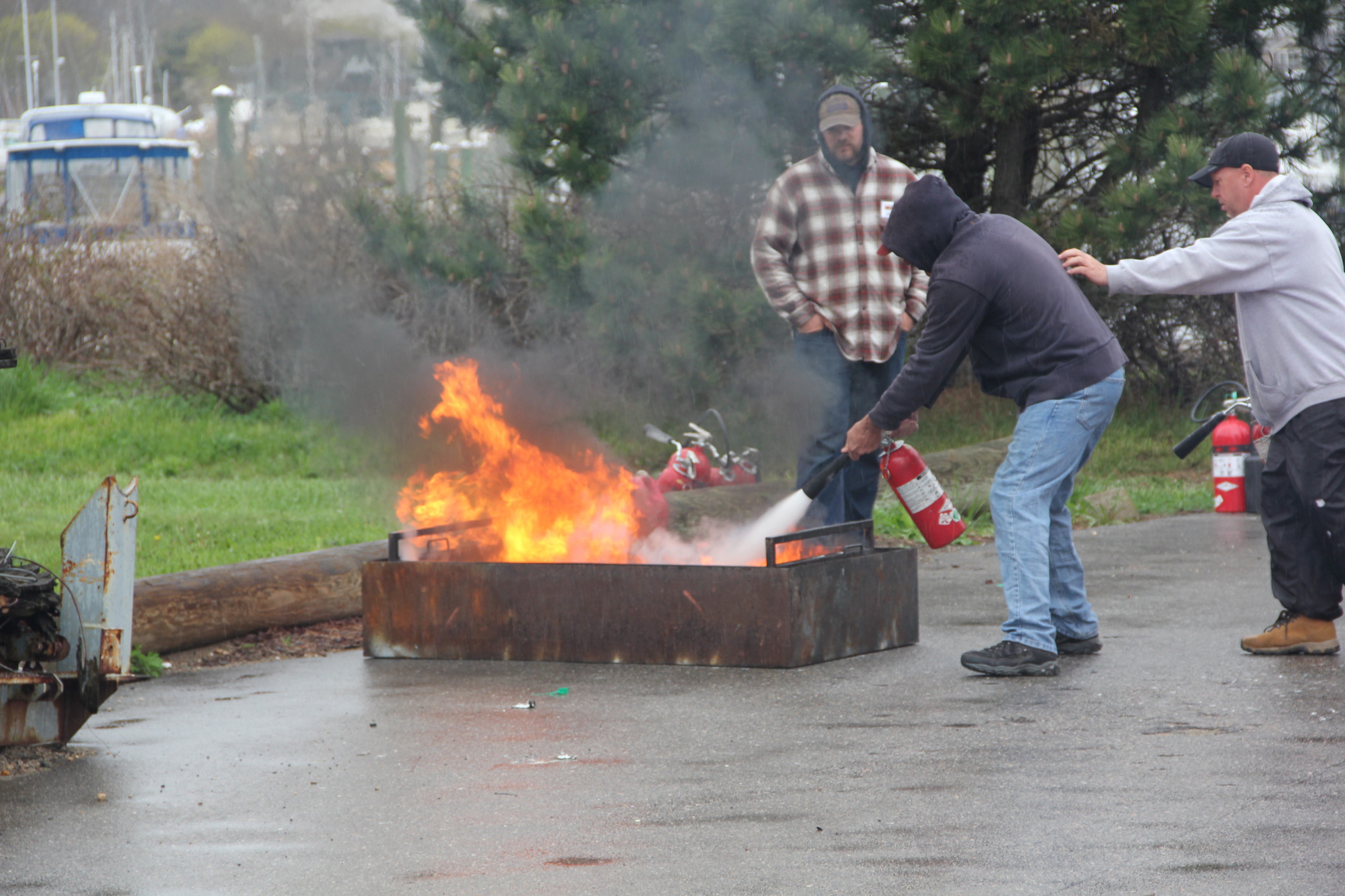 A fisherman practices fire suppression with a crew member providing backup